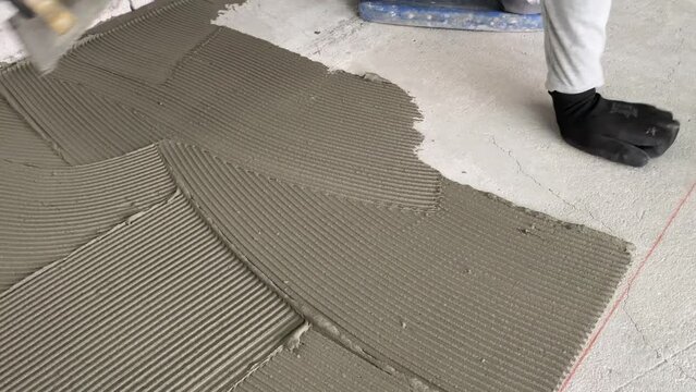 A builder applies tile adhesive to the floor. 4k video footage of construction work on laying tiles.