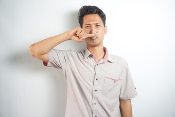 portrait of disgusted man pinches nose with fingers hands looks with disgust something stinks bad smell situation isolated on white wall background. Human face expression body language reaction