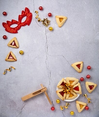 Hamantaschen Cookies, Triangular Pastry, Red Carnival Mask, Noisemaker on Gray Stone Table. Purim Celebration, Jewish Carnival Holiday Concept.