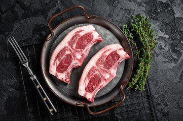 Raw fresh lamb loin chops with herbs and spices in steel tray. Black background. Top view