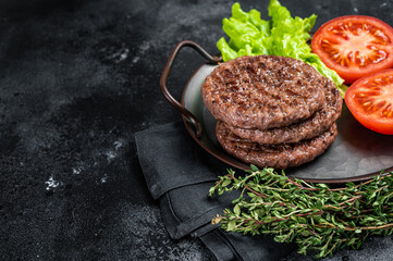 Tasty grilled burger beef patty with tomato, spices and lettuce in kitchen tray. Black background. Top view. Copy space