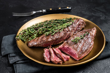 Fototapeta na wymiar BBQ grilled Bavette Bavet beef meat steak with herbs on a plate. Black background. Top view
