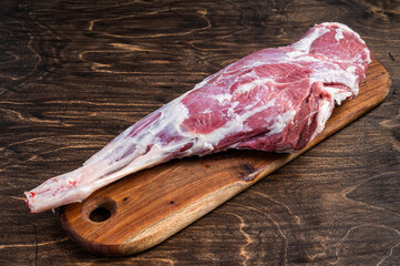 Mutton meat. Raw whole lamb leg thigh on butcher board. Wooden background. Top view