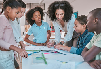 Female teacher in classroom with students, helping learner with homework and writing in book. Childrens education at school, educator reading kids notebook and group learning together for assessment - obrazy, fototapety, plakaty