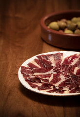 Iberian ham and olives on wooden table