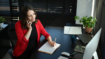 Attractive caucasian businesswoman in elegant red suit having pleasant conversation while sitting at workstation