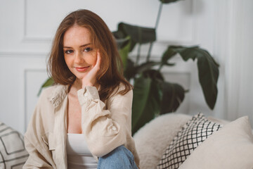 Portrait of beautiful cheerful redhead girl smiling looking at camera sitting on sofa at home