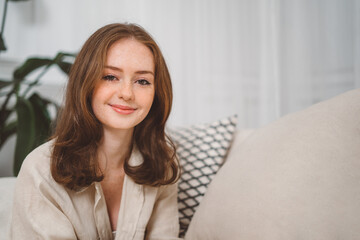 Portrait of beautiful cheerful redhead girl smiling looking at camera sitting on sofa at home