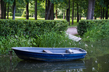 a blue boat stands on a pond in a park, a seagull sits on a boat, an old boat