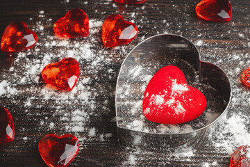 A metal mold for baking in the form of a heart on a dark wooden table sprinkled with flour. Gift...