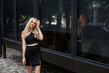 A stylish slender girl with blond long hair and a beautiful smile walks along the city street. Dressed in a short black sexy skirt and top.