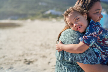 Portrait happy boy with Down Syndrome over shoulder of mother on beach