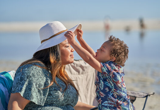 Curious son with Down Syndrome lifting mother's hat on beach