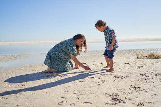 Mother and son with Down Syndrome drawing in sand with stick on beach