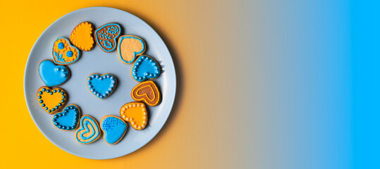 Cookies in shape of hearts decorated by yellow and blue icing and sprinkles on blue plate and yellow-blue background