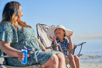 Mother watching happy cute son with Down Syndrome in hat on beach