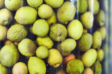 Close-up shot of a big glass jar full of green olives in brine