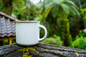 Enamel mug on the top of a fence with rain start poring and scenic view as the background