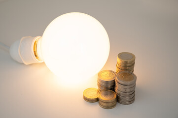Light bulb turned off, with stacks of coins next to it. Rising electricity tariffs, energy...