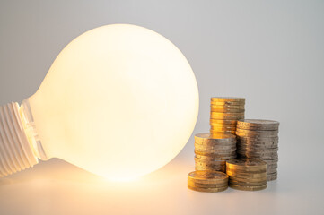 Light bulb turned off, with stacks of coins next to it. Rising electricity tariffs, energy...
