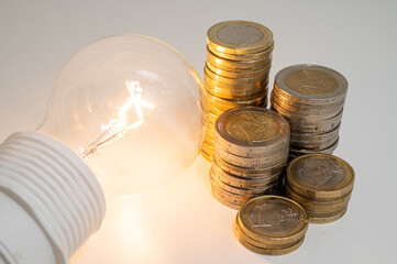 Light bulb turned off, with stacks of coins next to it. Rising electricity tariffs, energy...