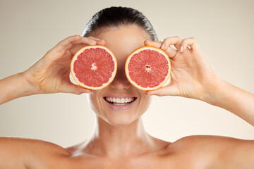Beauty, skincare and woman cover grapefruit for natural skin dermatology or cosmetic product. Vitamin c fruit on happy face aesthetic model in studio for sustainable self care for health and wellness