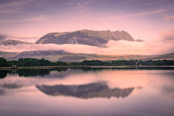 Spectacular reflection of the mountains on a lake with mist under the midnight sun, fairy tale...