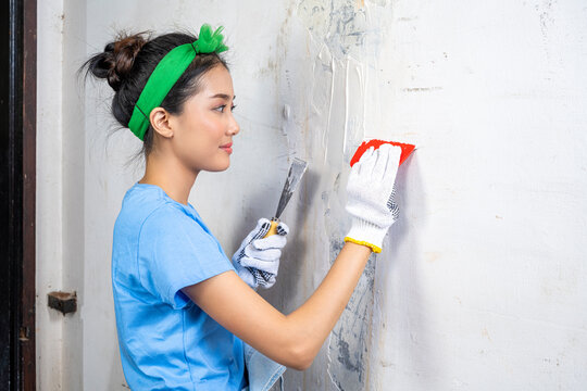 Asian young housewife in a glove holding a paint scraper and paint putty