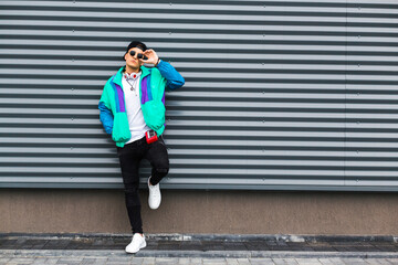 A young man in a sports jacket, cap, sunglasses with headphones and a player with batteries in the retro style of the 90s. Vintage look in modern fashion. The revival of old trends in a new way