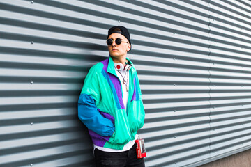 A young man in a sports jacket, cap, sunglasses with headphones and a player with batteries in the retro style of the 90s. Vintage look in modern fashion. The revival of old trends in a new way