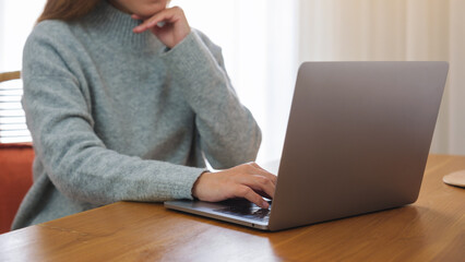 Closeup image of a young woman with chin resting, working on laptop computer at home