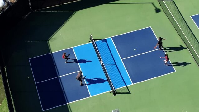 Pickleball foursome playing on sunny day hitting ball over net, aerial descending down over court
