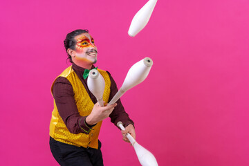 Clown with white facial makeup on a pink background, juggling maces