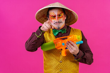 Clown with white facial makeup on a pink background, having fun with toy guns