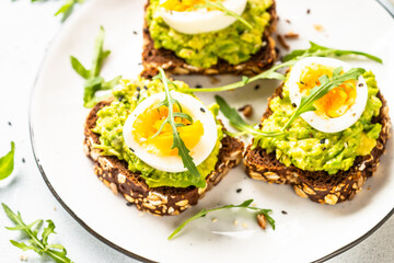 Avocado sandwich. Whole grain bread with avocado and boiled eggs with arugula. Close up image.