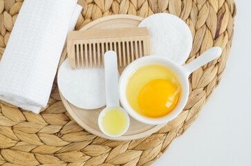 Small bowl with raw egg, small spoon with olive oil and wooden hairbrush. Homemade hair or face mask, natural beauty treatment and spa recipe. Top view, copy space.