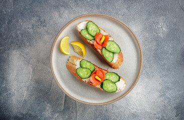 Salmon, cucumber and cream cheese sandwich with lemon in a gray plate on a concrete background.  Selective focus, top view and copy space - 564975345