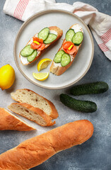 Salmon, cucumber and cream cheese sandwich with lemon in a gray plate on a concrete background.  Selective focus, top view - 564975347