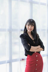 Cheerful Asian businesswoman smiling while standing with arms crossed Happy woman standing in meeting room of modern workplace vertical image