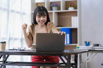 Portrait of happy businesswoman celebrating success with arms raised in front of laptop Asian woman wins lottery with fist raised arm with joy in the office