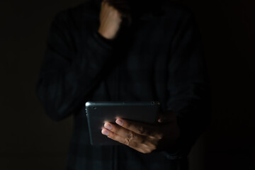 Cheerful bearded man in black long sleeve shirt using digital tablet in Dark room. hand holding tablet. 