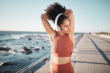 Beach, headphones and woman stretching for a fitness exercise, running or training for a race or marathon. Health, sports and female athlete doing an arm warm up before a cardio workout by the ocean. - obrazy, fototapety, plakaty
