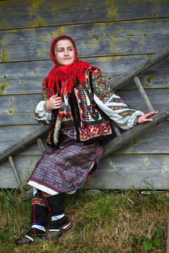 Ukrainian hutsul woman in authentic national costume sitting on a ladder near a wooden wall