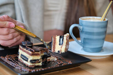 Unrecognizable woman eating a cake and drinking coffee in a cafeteria.