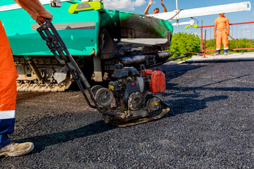 Worker compacts tarmac using vibration plate compactor