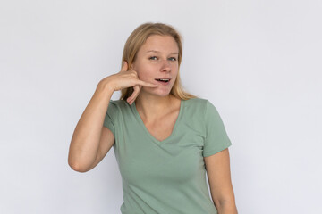 Pleased young woman showing call me sign. Portrait of happy Caucasian female model with fair hair in green T-shirt looking at camera, smiling, asking to call her. Advertising, support concept