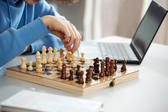Female teenager play chess with himself. Closeup hand hold pawn. Home hobby, learning to play chess with laptop from Internet.