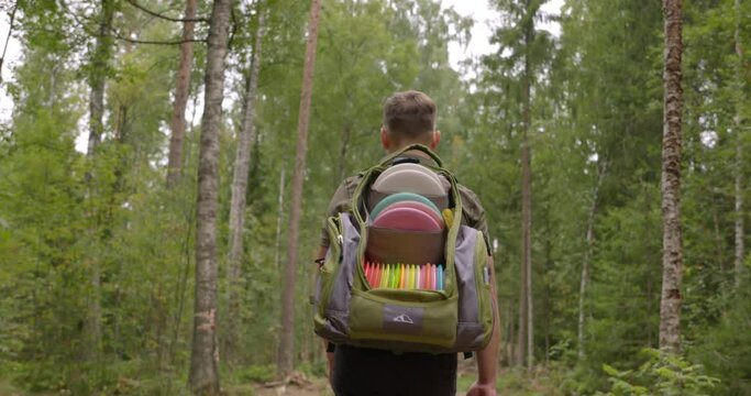 Disc golfer walks on a disc golf course in the forest - medium shot
