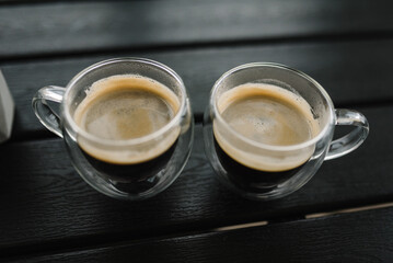 Two cups of hot black coffee on dark wooden table. Ground or instant coffee. Delicious and strong aromatic Americano or espresso coffee. Cups glass transparent on dark background. Top view. Copy space