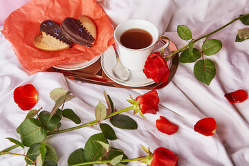 St Valentines breakfast in bed among red traditional roses - vegan heart shaped cookies and coffee cup on the sheets. Aesthetics, romantic lagom holiday background.
